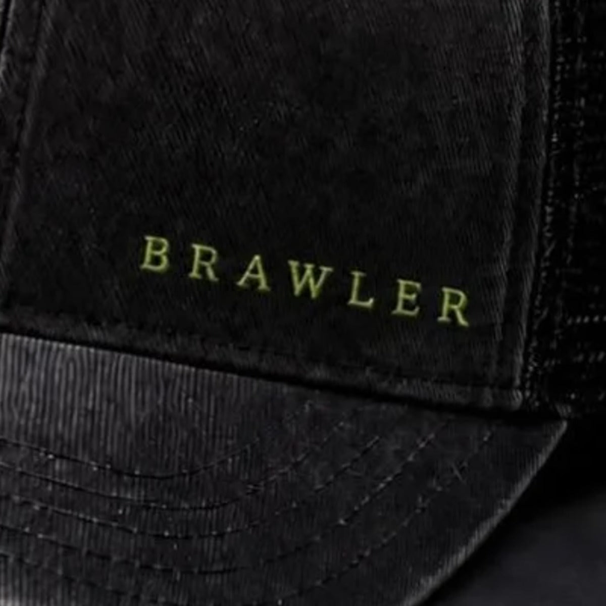 Close-up of lime BRAWLER embroidery stitched into washed black cotton